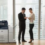 Zwei Personen in Geschäftskleidung diskutieren Dokumente in einem Büro neben einem Multifunktionsdrucker der Serie Xerox® AltaLink® B8200